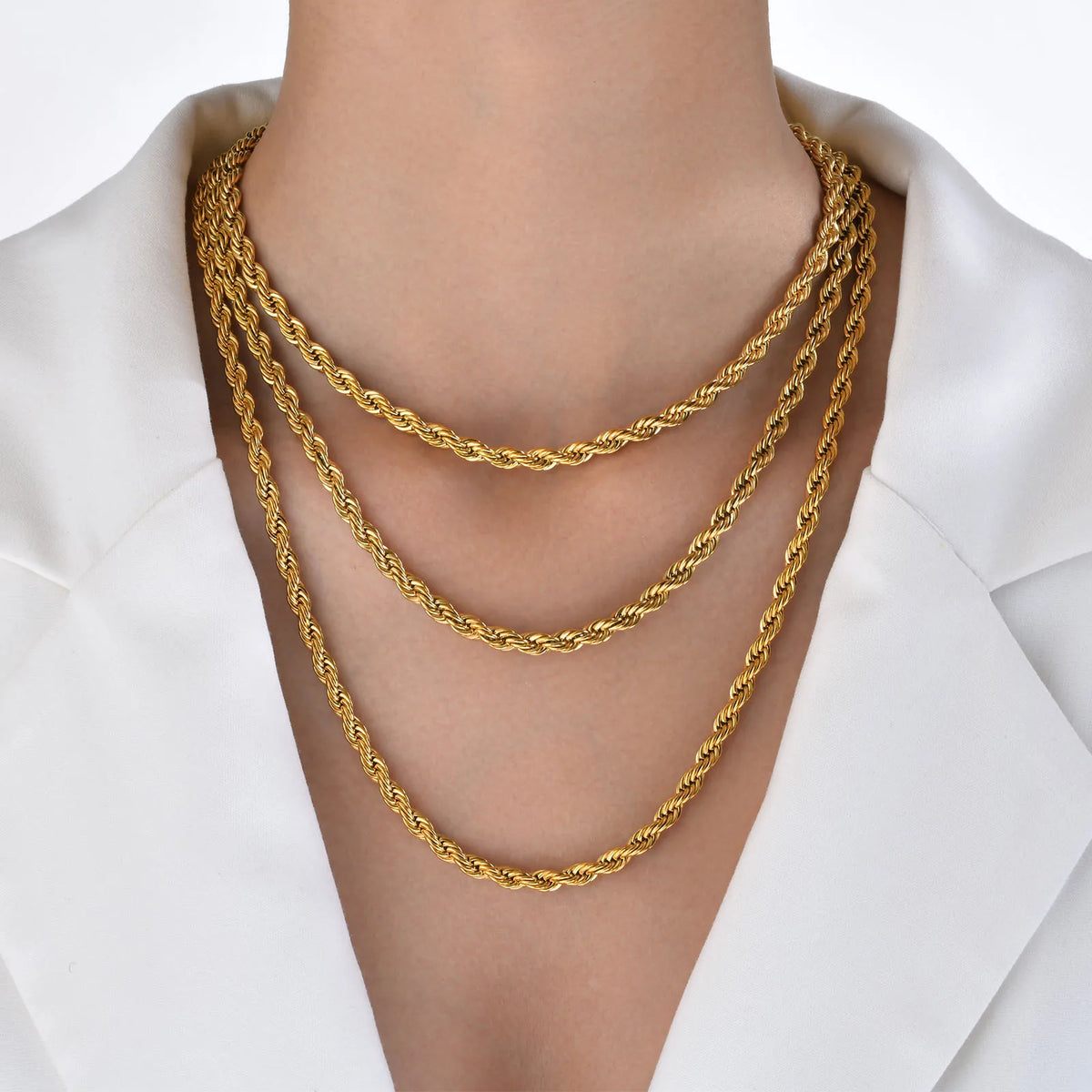 A close-up of a dainty gold rope chain necklace worn around the neck against a white background.