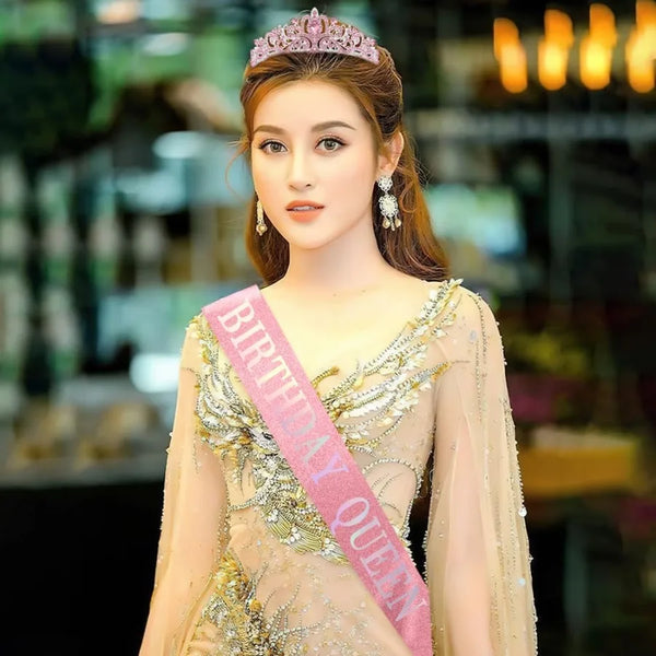 A young woman wearing a pink crown and a sheer gold gown with rhinestone detailing.