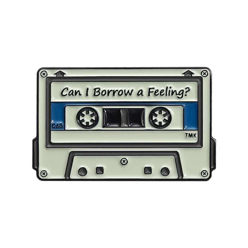 A vintage cassette tape enamel pin brooch with a rectangular body and a label reading Can I Borrow a Feeling?