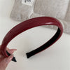 A maroon PU leather fashion headband is shown against a light gray background.