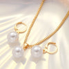 A delicate gold necklace with a pearl pendant and matching hoop earrings displayed on a light background.