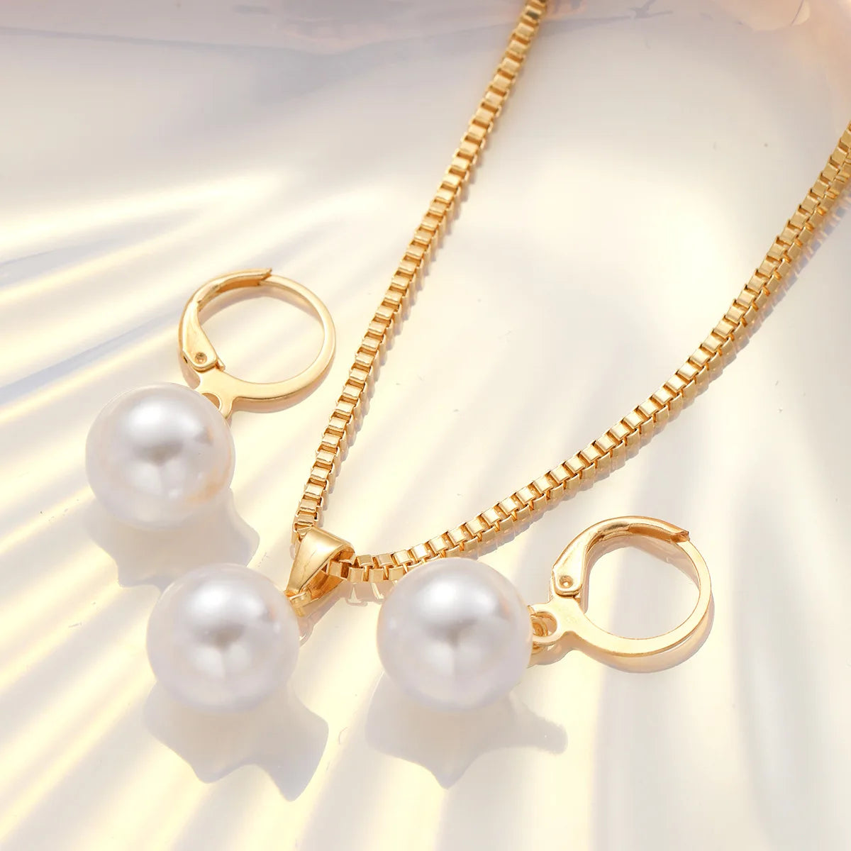 A delicate gold necklace with a pearl pendant and matching hoop earrings displayed on a light background.