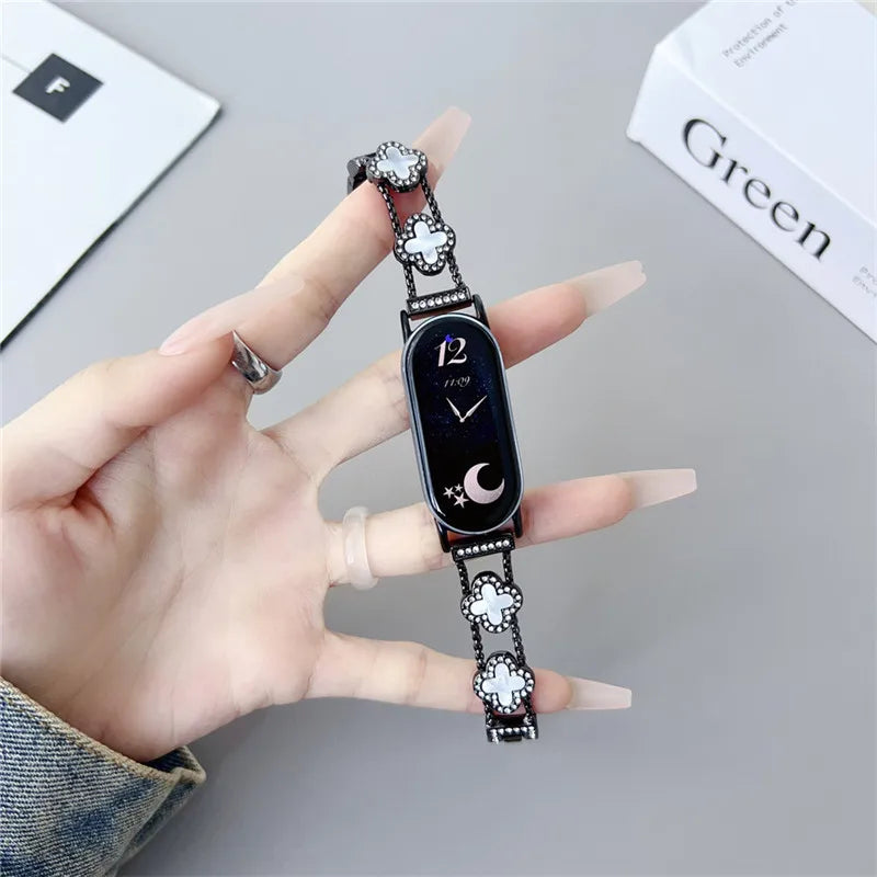 A hand holds a black digital watch strap with silver accents and a moon symbol, displayed next to a green box.