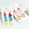Un par de pendientes colgantes con forma de las letras I, Z, A, B y C en esmalte rosa, blanco y amarillo.