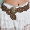 A brown leather and brass retro western cowboy round hollow metal belt worn over a white lace skirt.