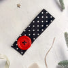 A black fabric headband with white polka dots and a red button detail is displayed on a white surface.