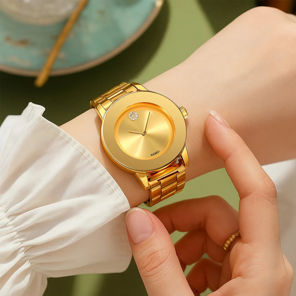 Primer plano de un reloj de pulsera de cuarzo tono dorado, llevado en una muñeca, con la manga de una camisa blanca visible.