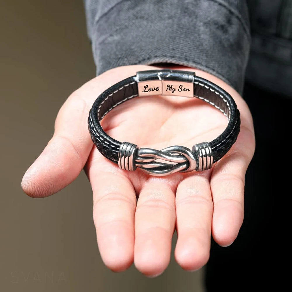 A hand holds a personalized leather knot bracelet with the inscription Love My Son.
