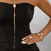 A woman wearing a black dress and gold baroque imitation pearl jewelry set with a long pendant necklace and a ring.