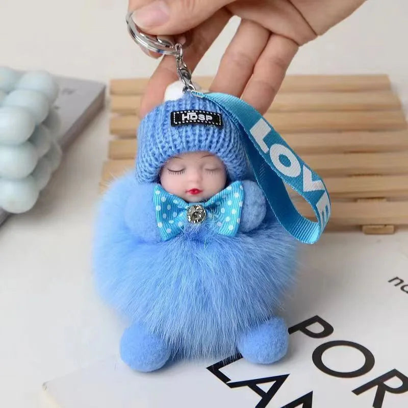 A fluffy blue cartoon plush doll with a knitted hat and bow, attached to a silver keychain.
