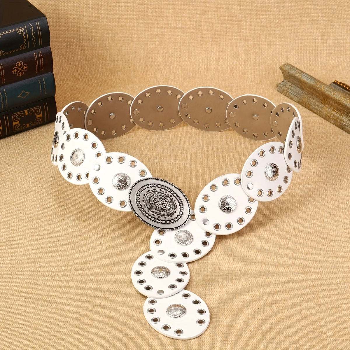 A close-up of a unisex floral oval waist belt made of silver and gold-toned metal discs on a beige fabric background.
