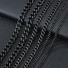 A close-up of multiple black Cuban link chains laid diagonally on a dark surface.
