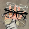 A hand holds a pair of classic black square-framed eyeglasses with clear lenses.