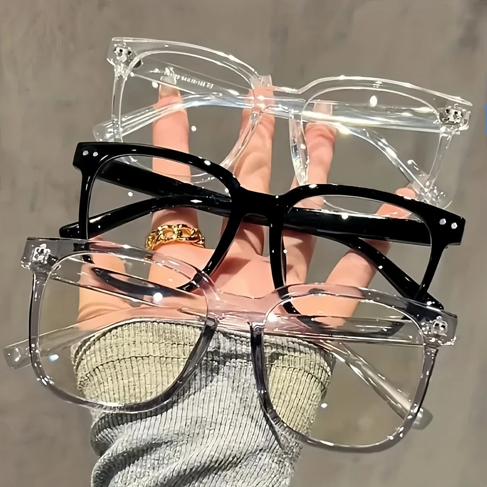 A hand holds a pair of classic black square-framed eyeglasses with clear lenses.