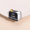 A black and white enamel pin featuring a duck illustration and the text Live Laugh Toaster Bath
