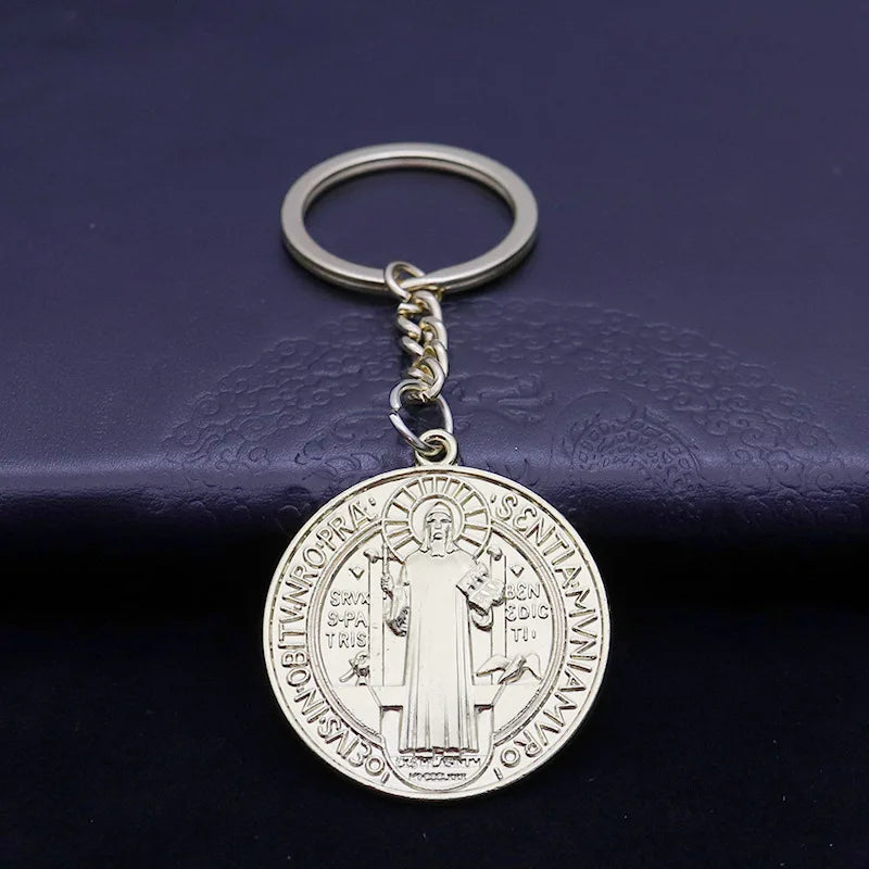 A round silver medallion keychain featuring a depiction of St. Benedict.