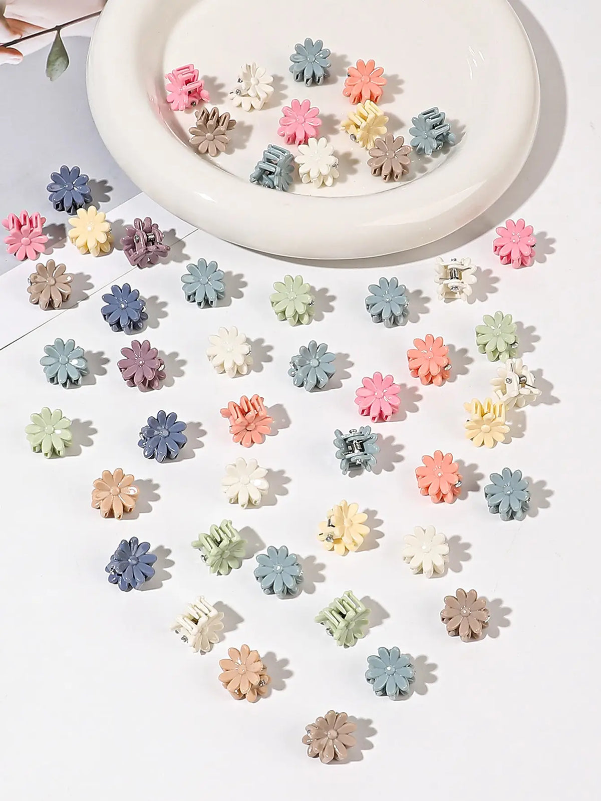 A collection of colorful mini flower hair clips in various shades of pink, purple, green, and beige arranged on a white plate