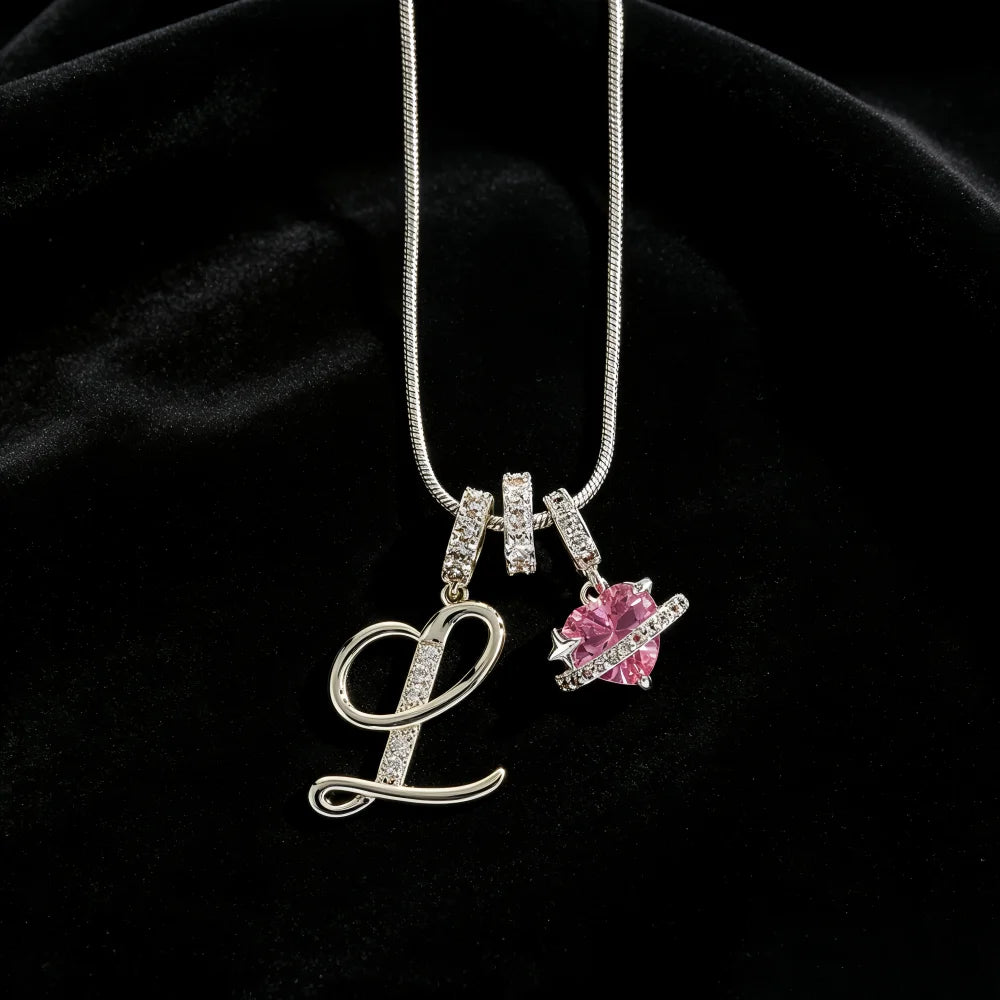 A silver alphabet L pendant necklace featuring a pink gemstone flower charm on a black velvet background.