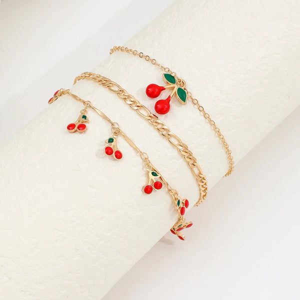 Un ensemble de bracelets de cheville dorés avec de petites perles en forme de cerises rouges et vertes.
