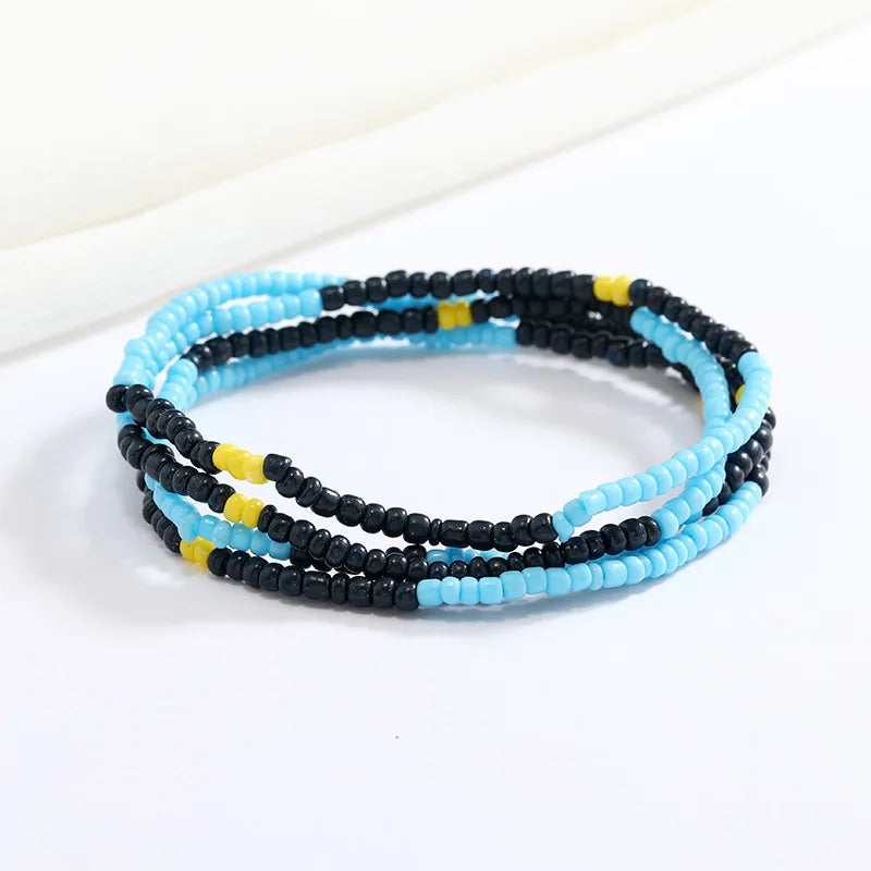 Una pila de pulseras de cuentas negras, azules y amarillas sobre un fondo blanco.