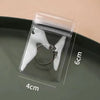A clear self-sealing jewelry storage pouch containing a silver ring, shown on a dark gray plate.