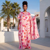 Une femme modèle un foulard floral rose avec des motifs de cœurs en extérieur sur un fond architectural blanc.
