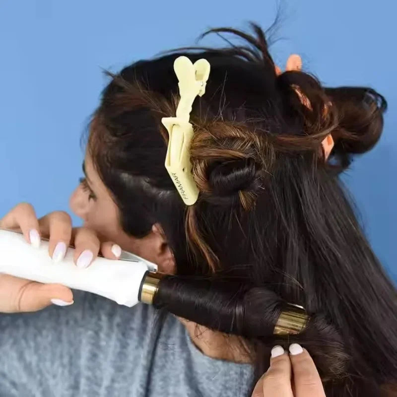 A person is using a white hair iron on their dark hair while a yellow alligator hair sectioning clip is visible in the hair.