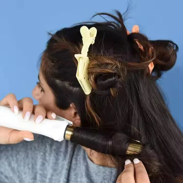 A person is using a white hair iron on their dark hair while a yellow alligator hair sectioning clip is visible in the hair.