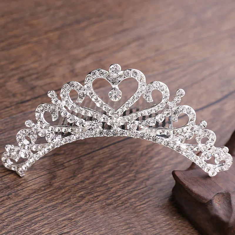 A sparkling crystal princess tiara hair comb for women displayed on a dark wooden surface.