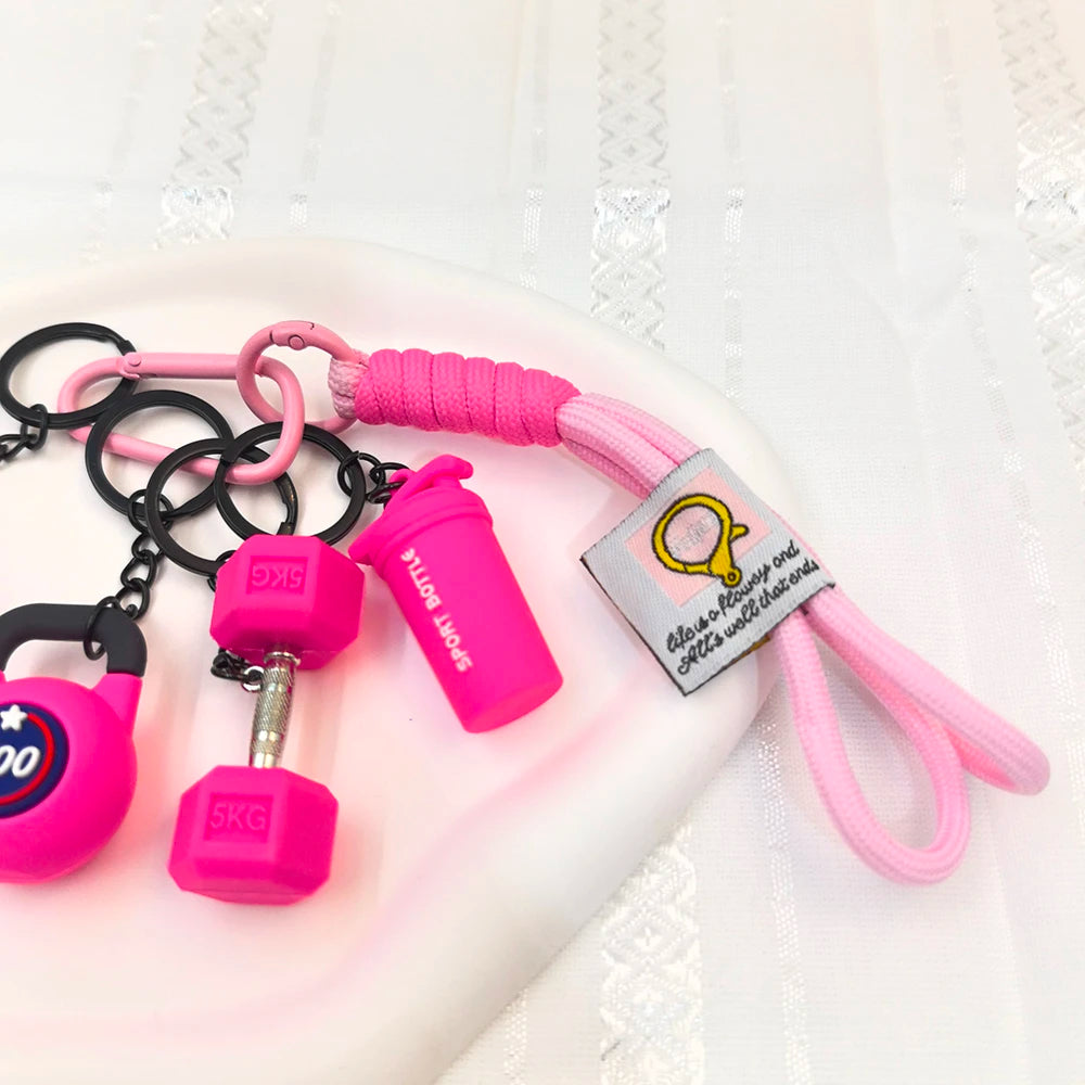 A collection of pink and black fitness keychains and weightlifting accessories including dumbbells and resistance bands.
