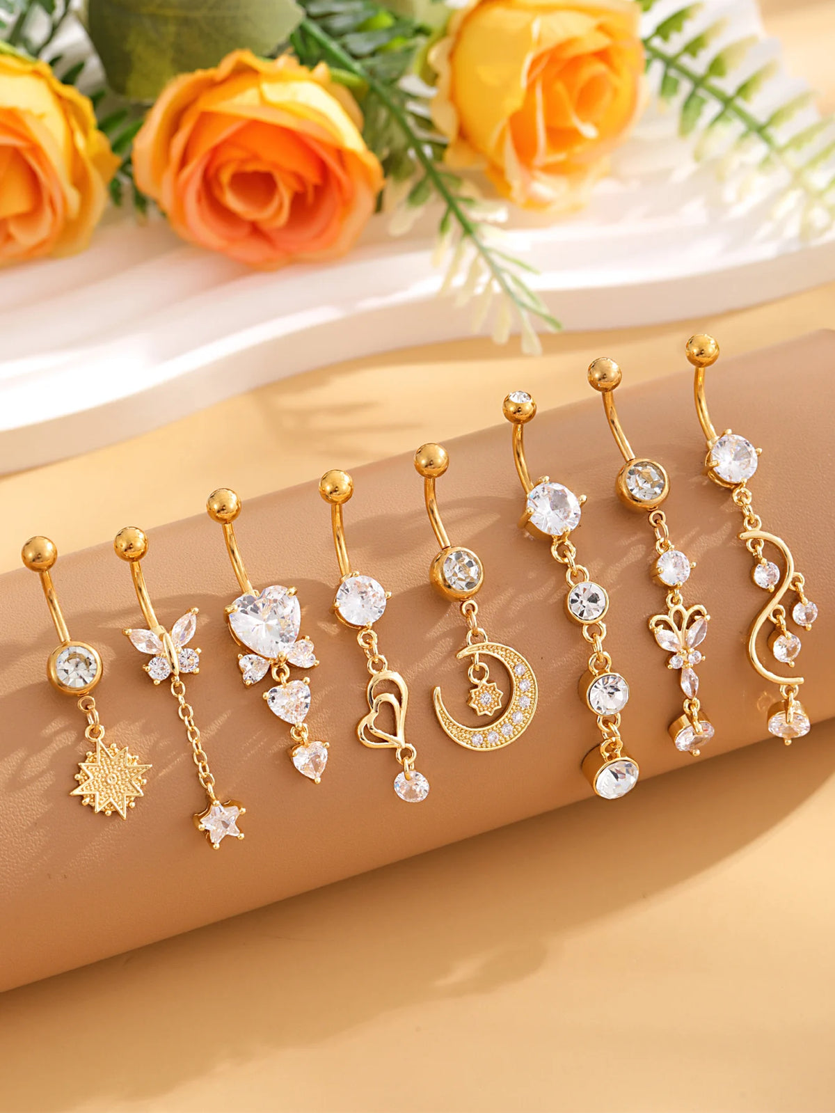 A set of gold dangle curved belly piercing jewelry featuring heart, flower, and crescent moon charms.