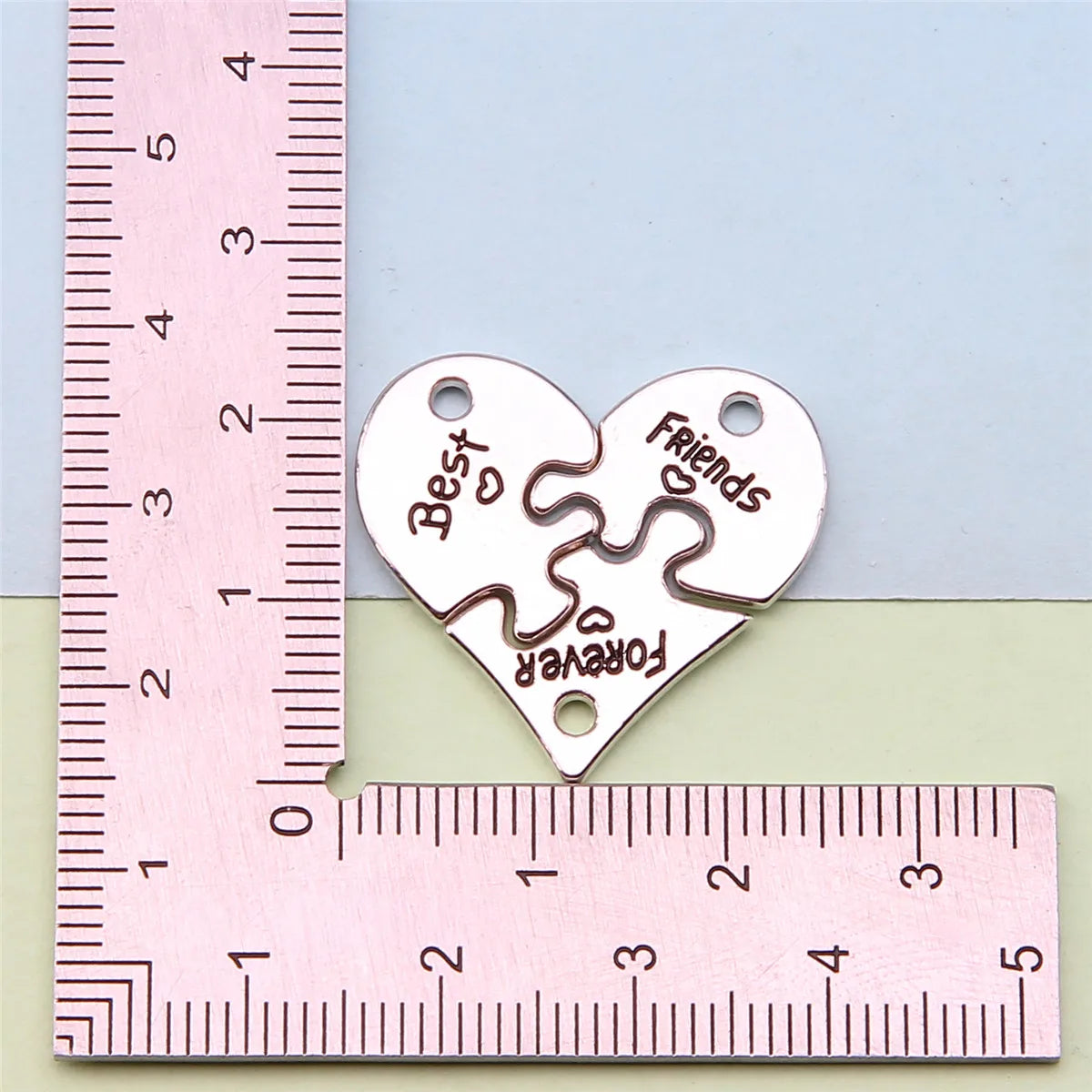 Colgante de corazón plateado con las palabras 'Best Friends Forever' grabadas, medido con una regla.