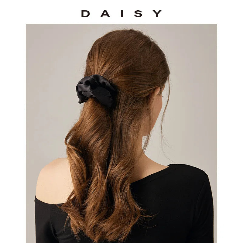 A woman with long brown hair styled in a low ponytail secured with a black satin elastic hair tie.