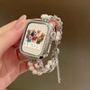 A hand holds a square digital watch with a silver casing and a beaded strap, displaying the time 16:05.