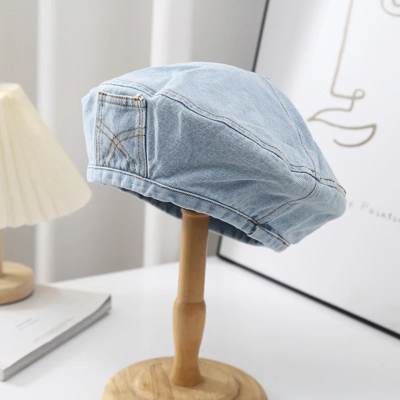 A light blue retro washed cotton denim beret hat displayed on a wooden stand.