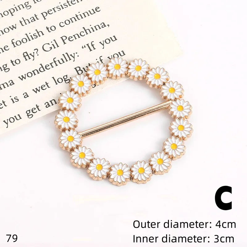 A gold-toned button clip made of white and yellow floral rhinestones is shown against a piece of paper.