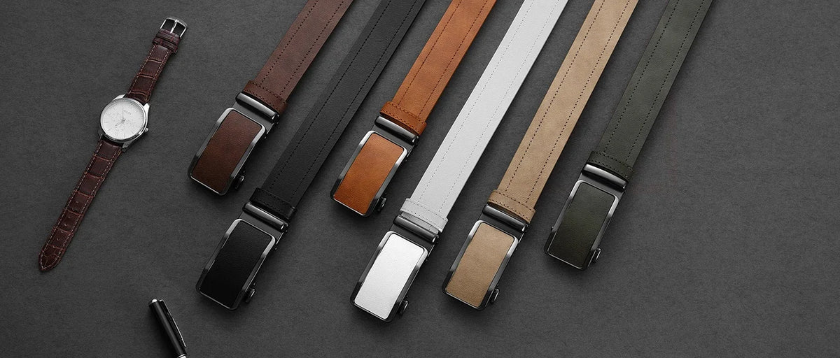 A collection of men's leather belts in various colors and finishes laid diagonally on a dark surface.
