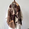 A beige and brown plaid cashmere scarf draped over a white top, displayed on a hanger.