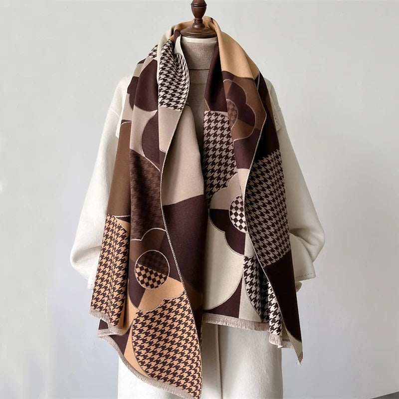 A beige and brown plaid cashmere scarf draped over a white top, displayed on a hanger.