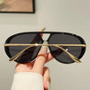 A hand holds a pair of black aviator style UV protection sunglasses with gold accents.