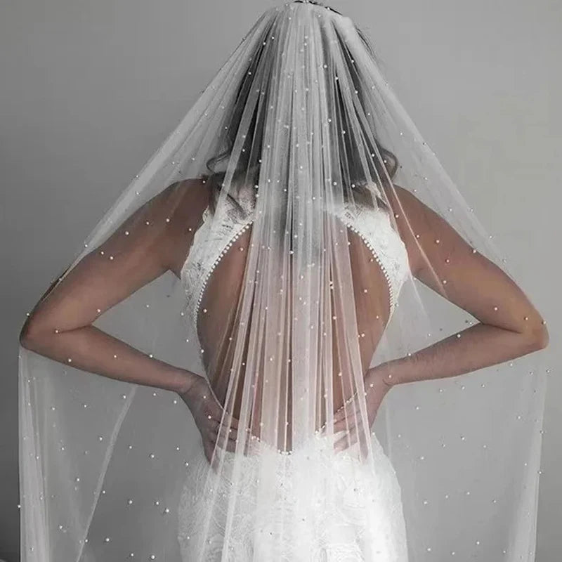 Vista trasera de una novia con un velo nupcial de perlas transparentes y un peine sobre su cabello y vestido de novia blanco