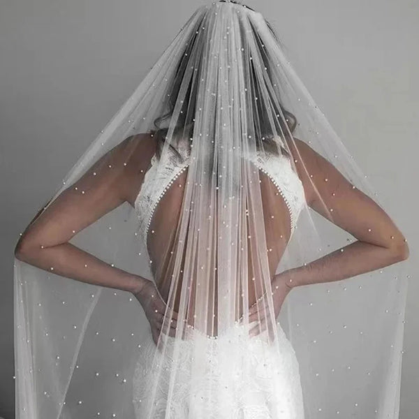 Vue de dos d'une mariée portant un voile nuptial en perles transparentes avec une peigne dans ses cheveux et une robe de mari