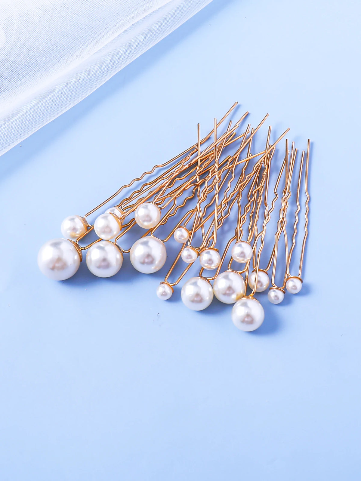 A collection of 18 faux pearl hair pins with thin metal wires arranged diagonally on a light blue background.