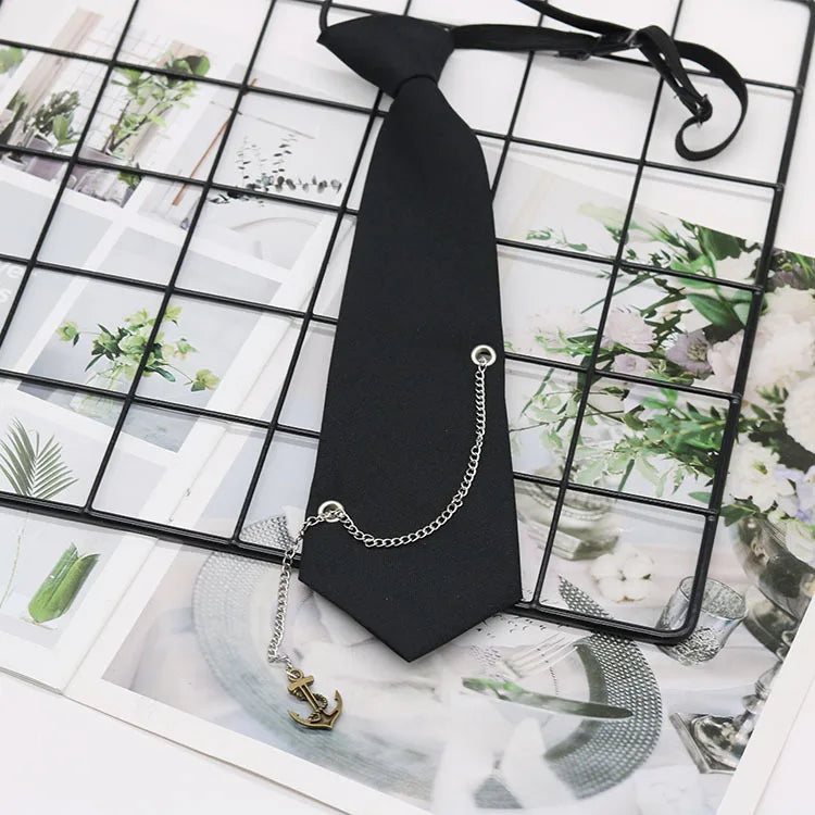 A black necktie with a silver chain attached, displayed on a grid background featuring floral and botanical prints.