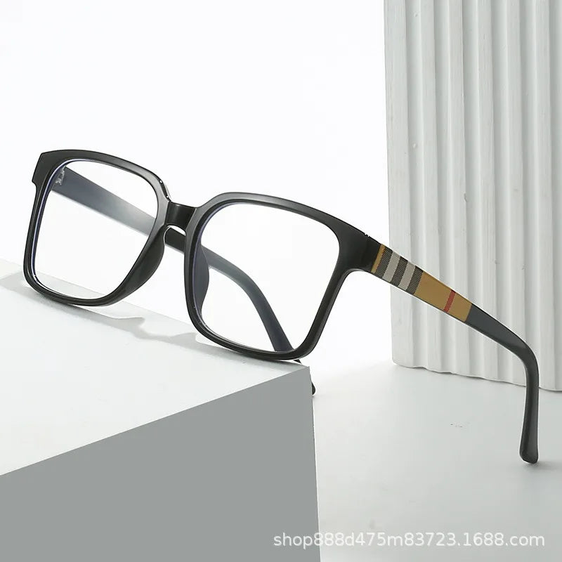 Black rectangular eyeglasses with a tortoiseshell accent on the temple, resting on a white surface.