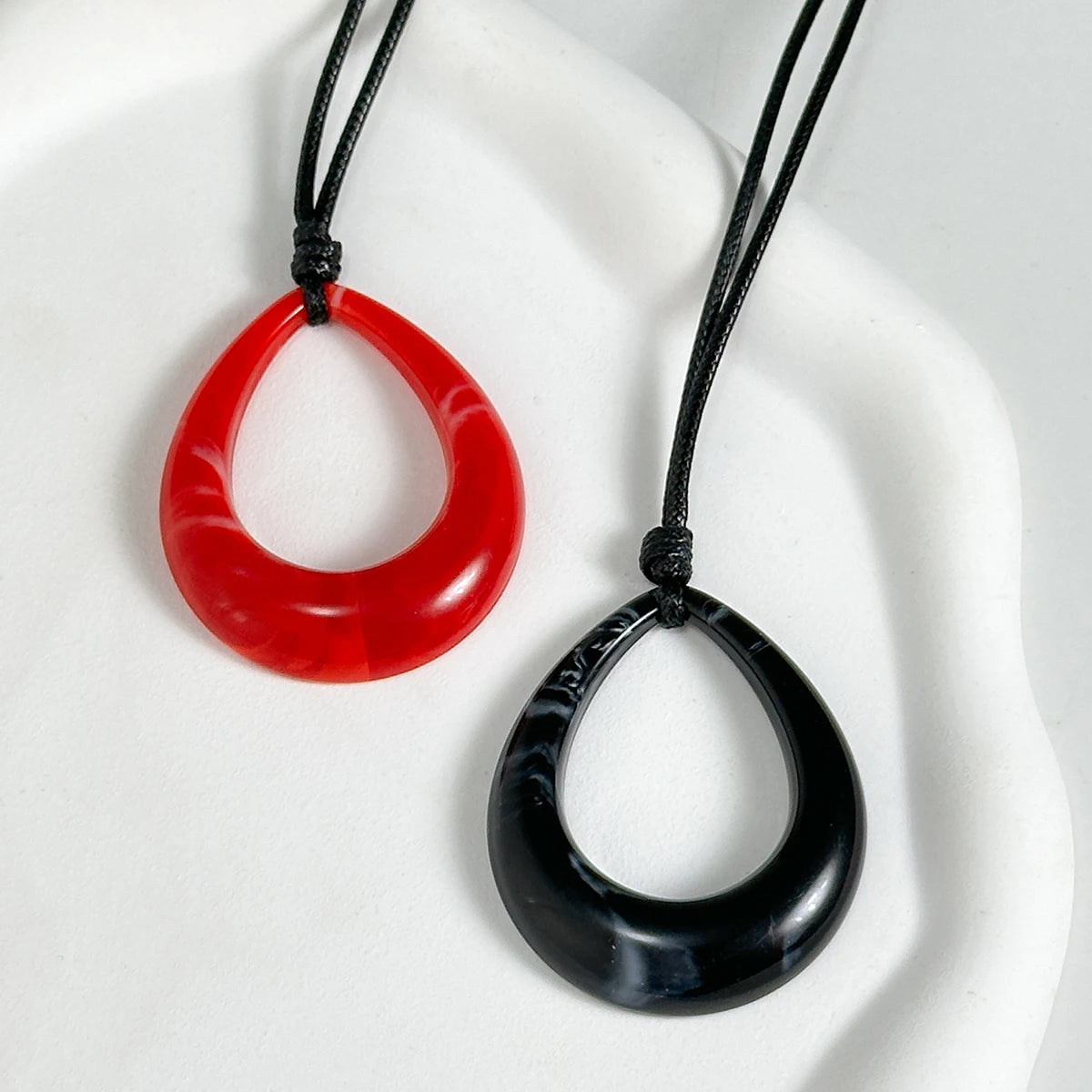 A pair of necklaces featuring a red and black oval pendant on black cord against a white background.