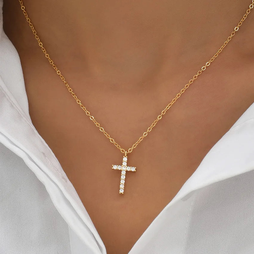 Gold chain necklace with a zircon cross pendant worn against a white shirt.
