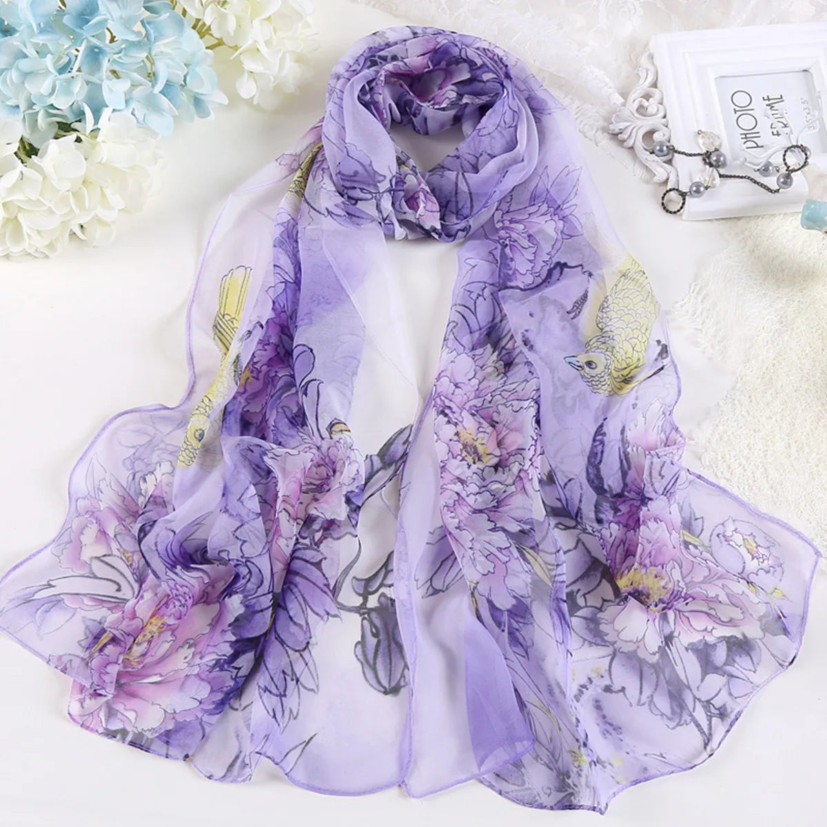 Étole de soie florale violette transparente avec des fleurs lavande et lilas, présentée sur une surface blanche.