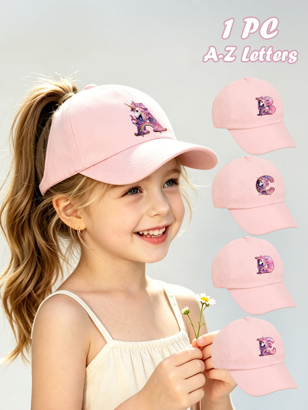 A young girl is smiling while wearing a pink unicorn letter baseball cap and holding several other letters.