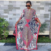 Eine Frau in einem farbenfrohen, bohemienartigen Seidendruck-Kaftan steht draußen vor einer strukturierten Wand.